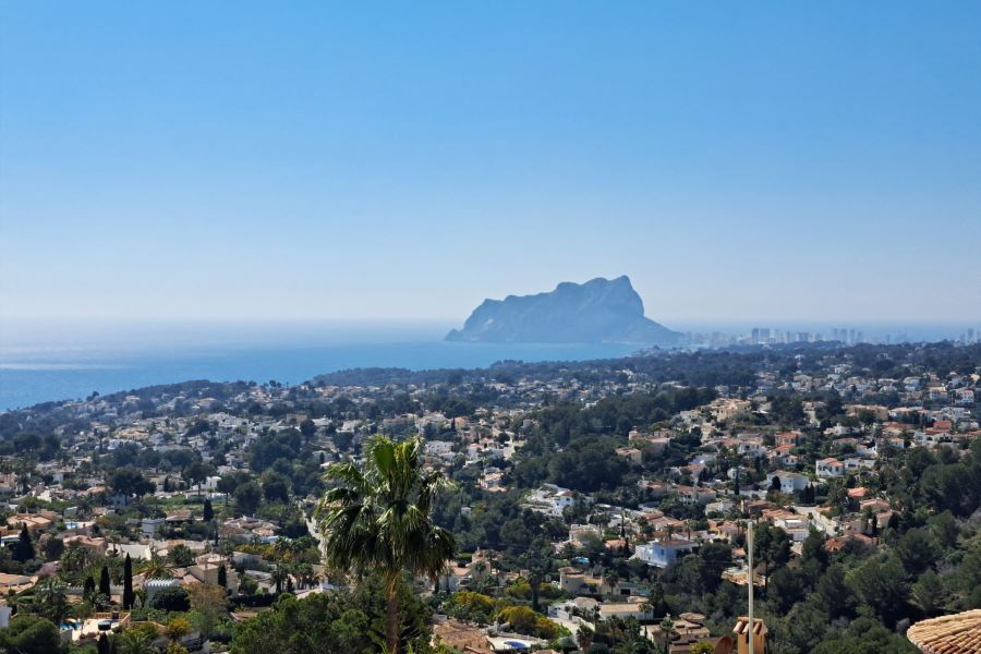 Panoramic elevated view of Benissa Costa residential area with luxury villas, Mediterranean vegetation, and the iconic Peñón de Ifach rock on the skyline under a clear blue sky