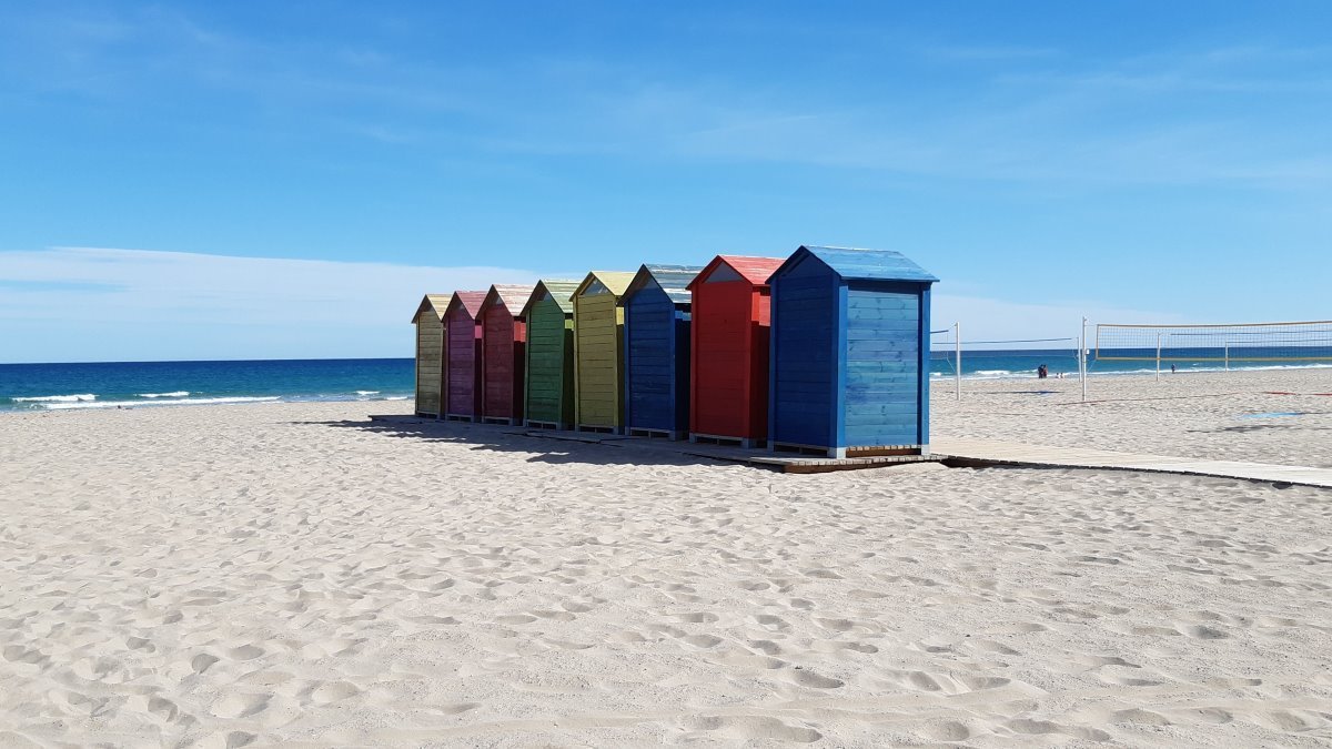 Row of vibrant colorful wooden beach huts on the sandy shore of Playa de San Juan in Alicante under a clear blue sky